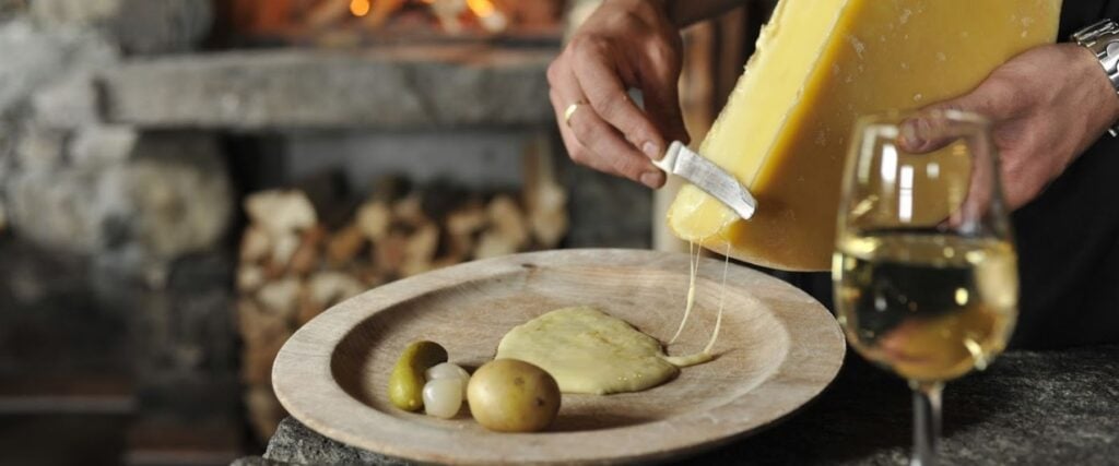 A cheese raclette being scraped onto a plate